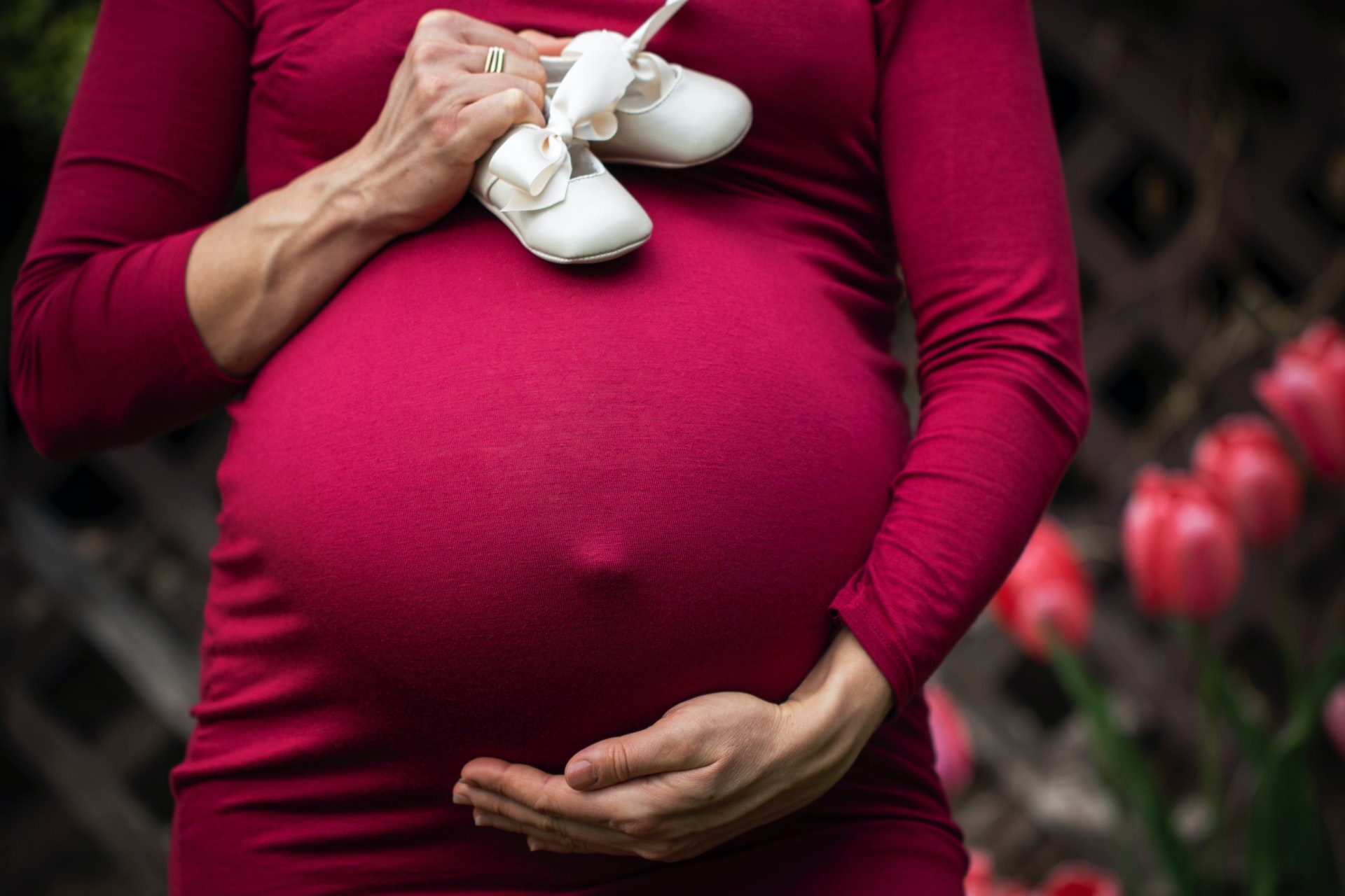 A pregnant woman in a red dress cradling her belly.