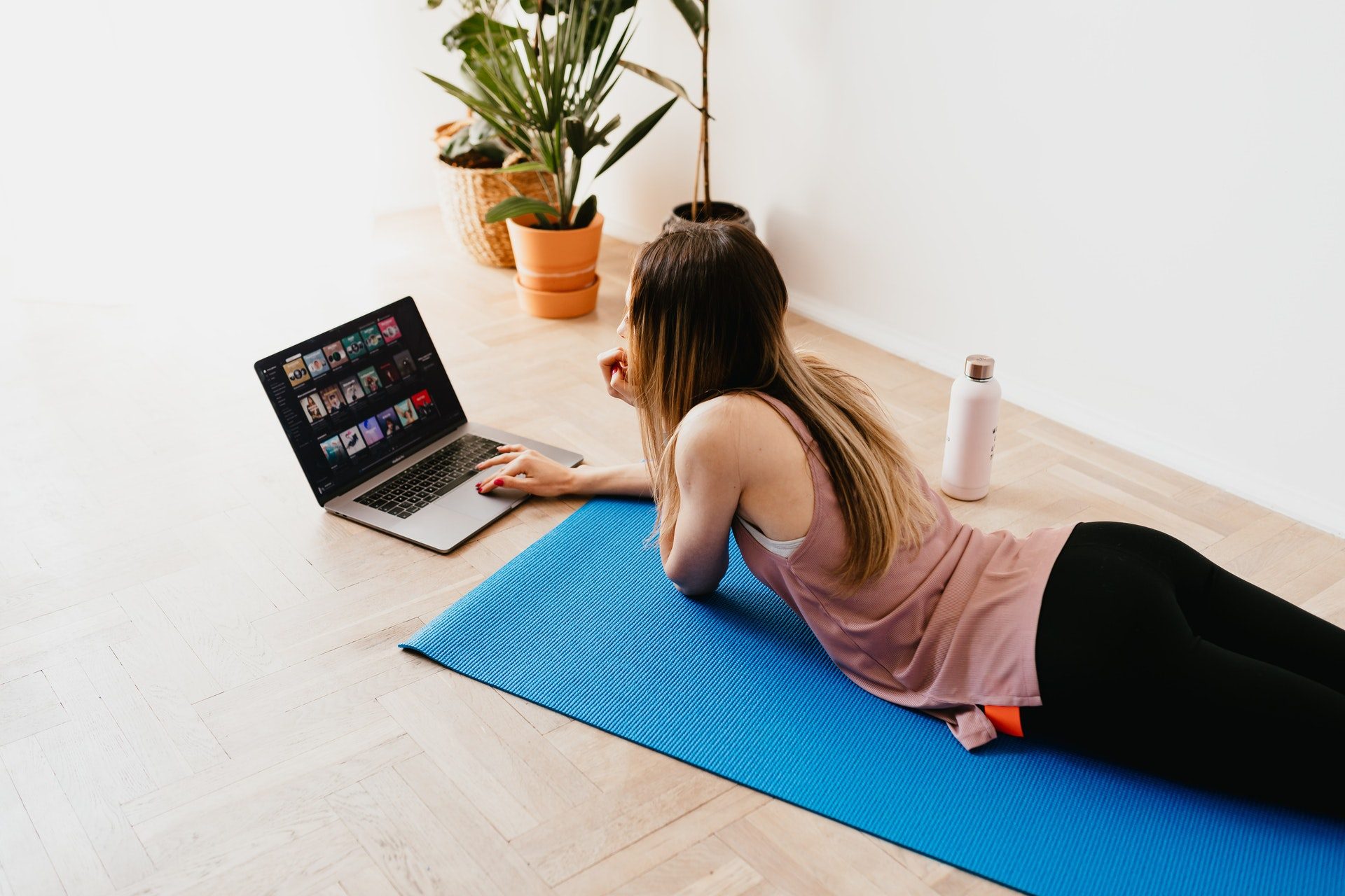Dark haired woman watching workout videos on a blue yoga mat.