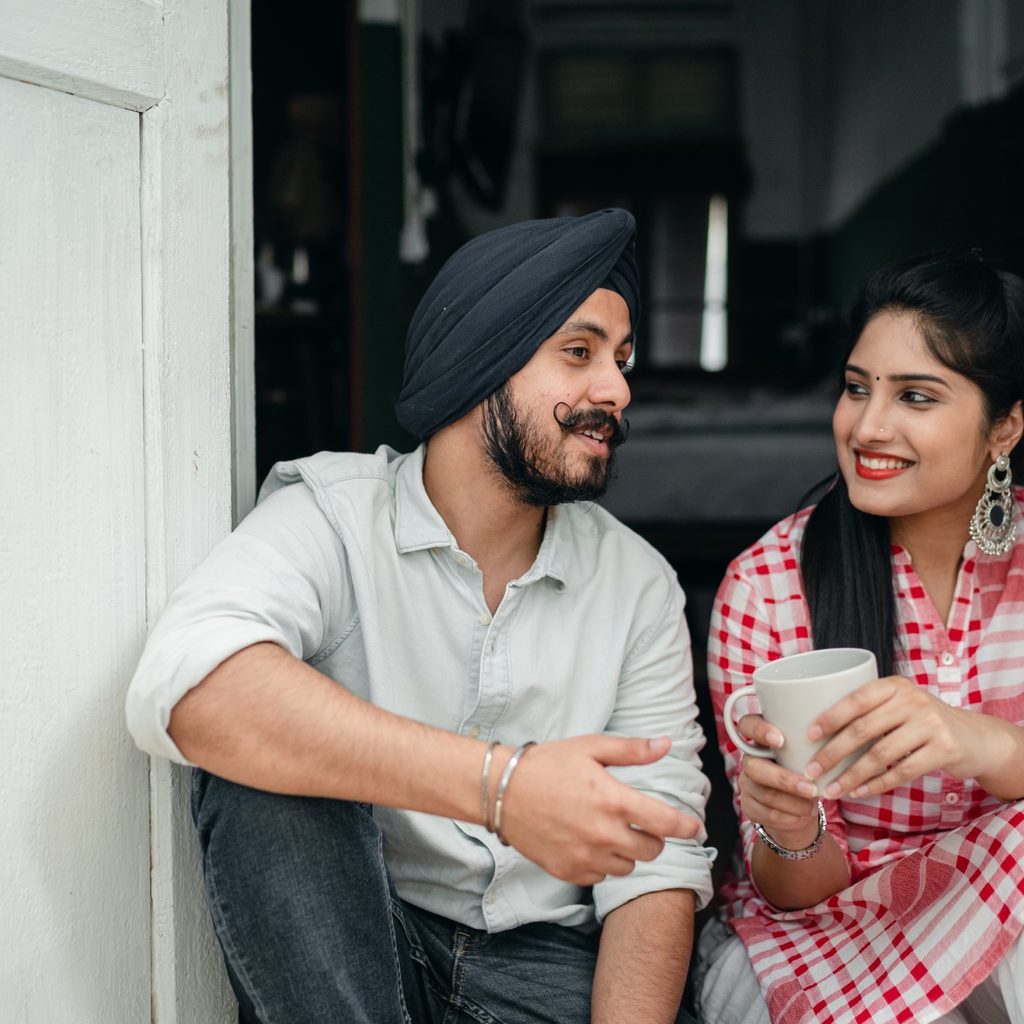 a young couple sits outside chatting and smiling while the woman holds a coffee mug
