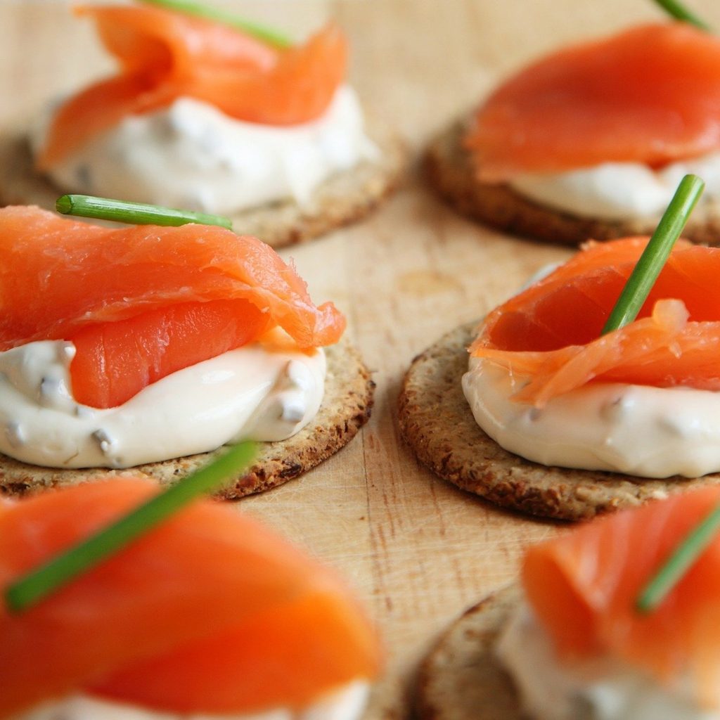 six crackers with cream cheese spread, salmon, and and herb garnish on a wooden counter