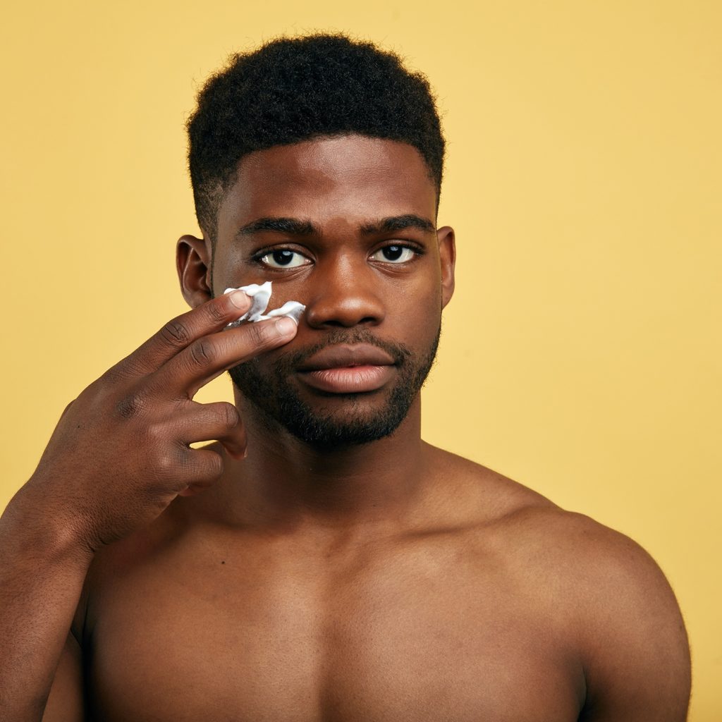 shirtless man applying lotion to his face
