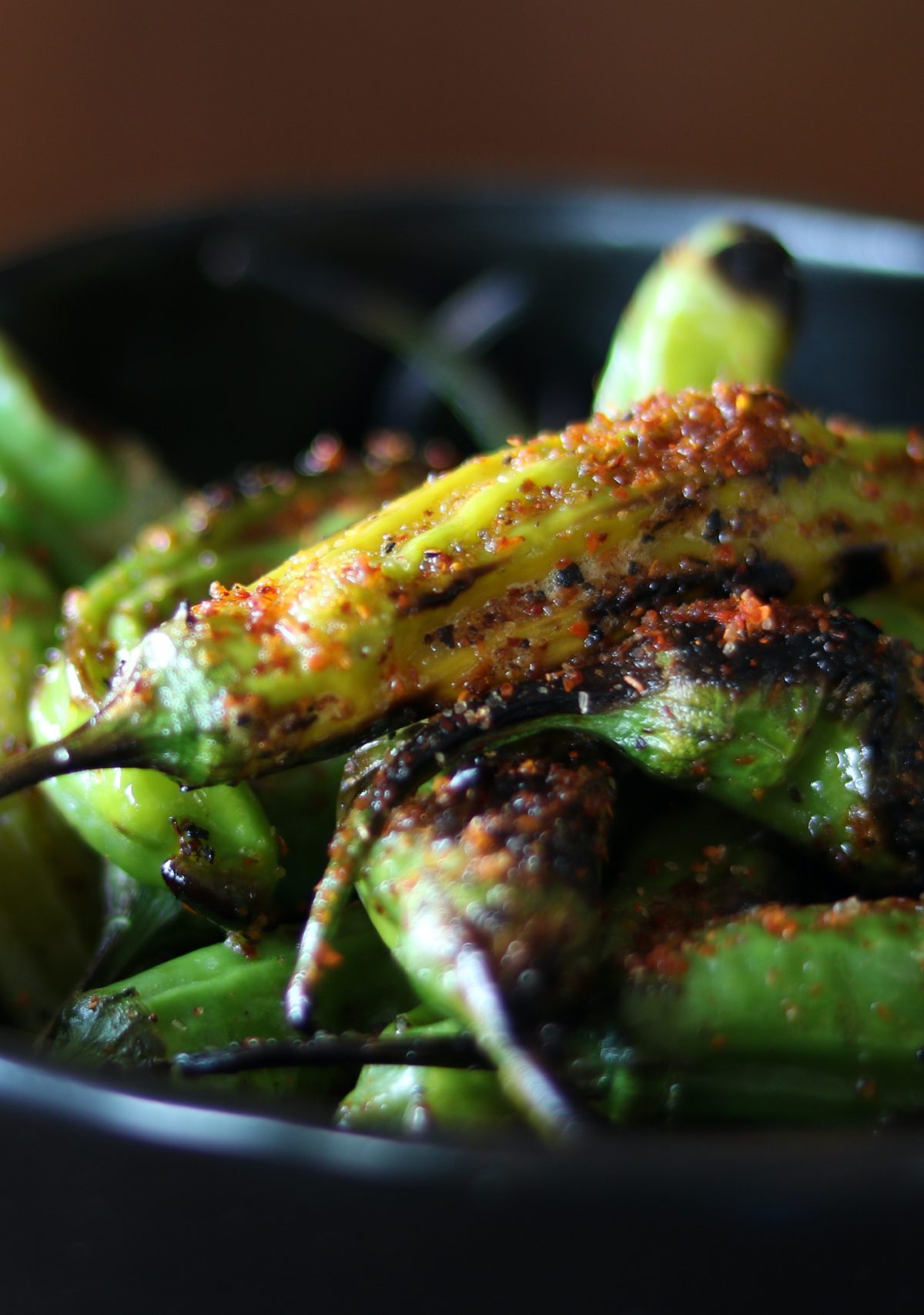 a black bowl of green blistered shishito peppers