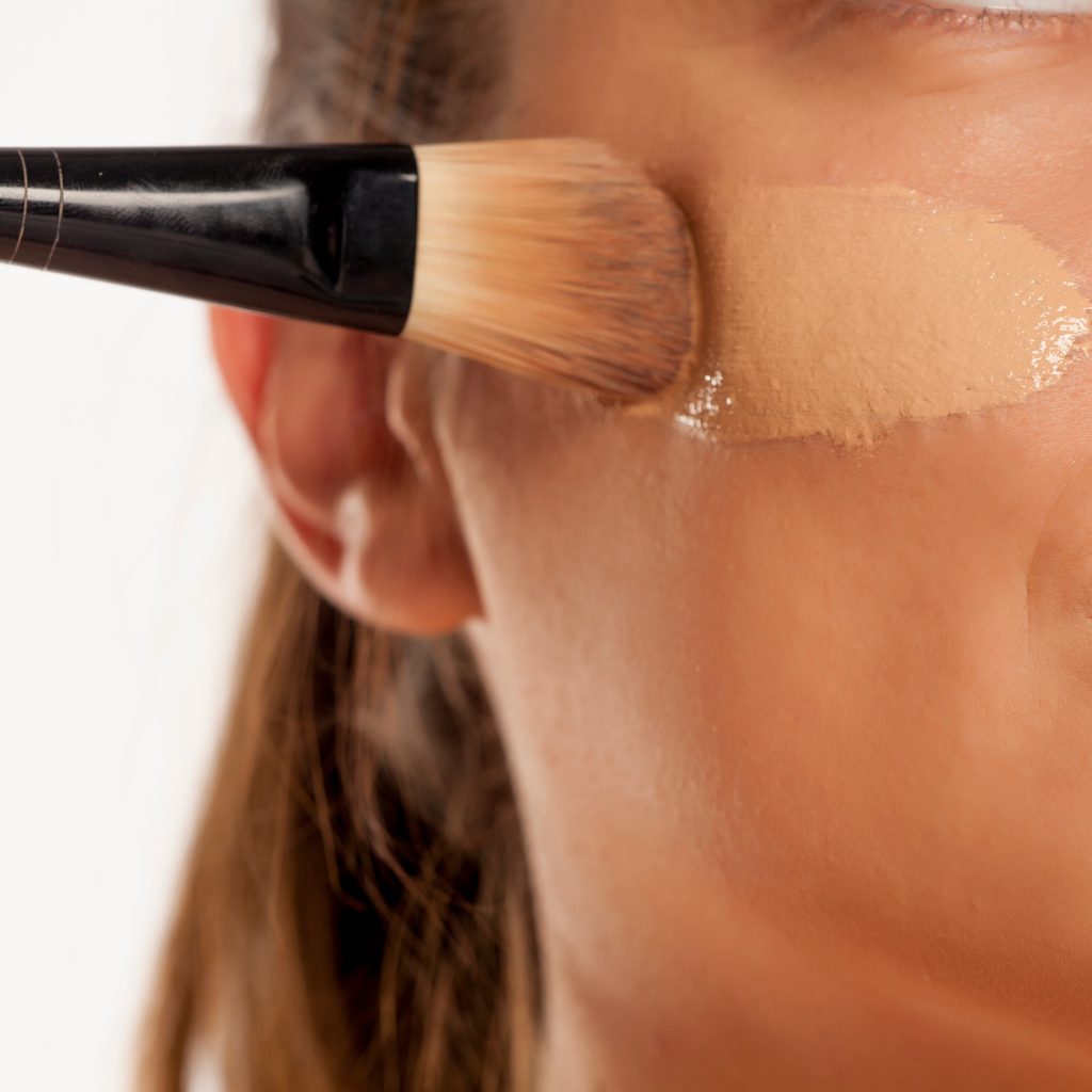 woman applying foundation to cheek with brush
