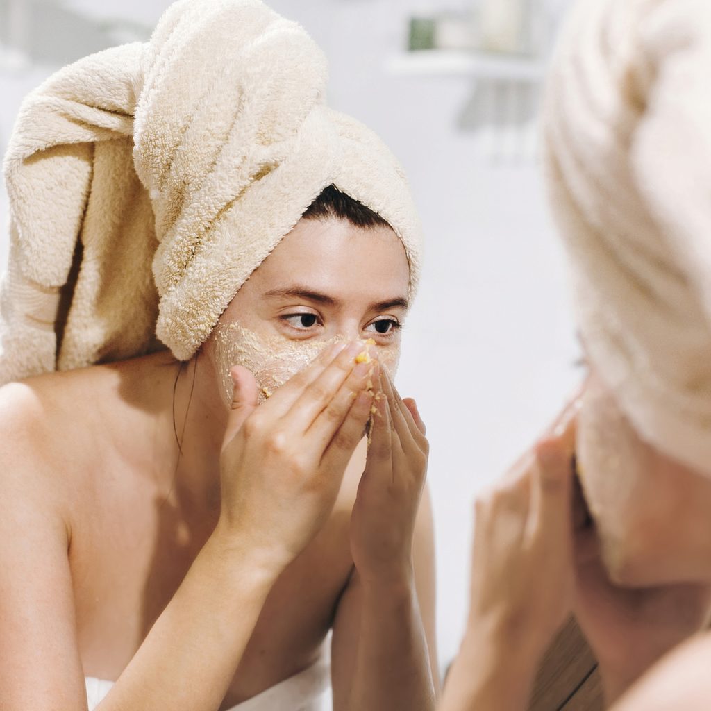 woman wearing towel exfoliating her skin in bathroom