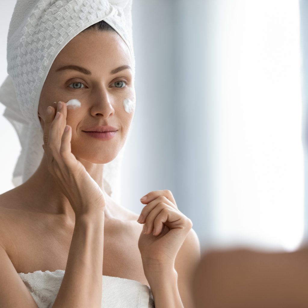woman applying moisturizer in mirror