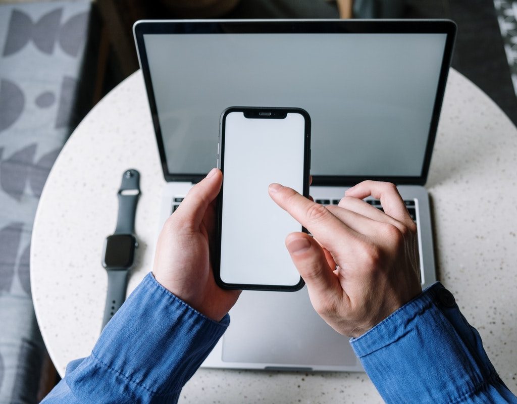Someone on their iPhone with their Apple Watch and laptop on a table