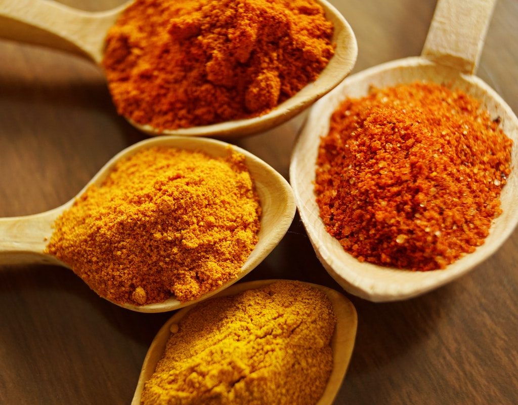 Bright orange and yellow spices, like turmeric, in different spoons