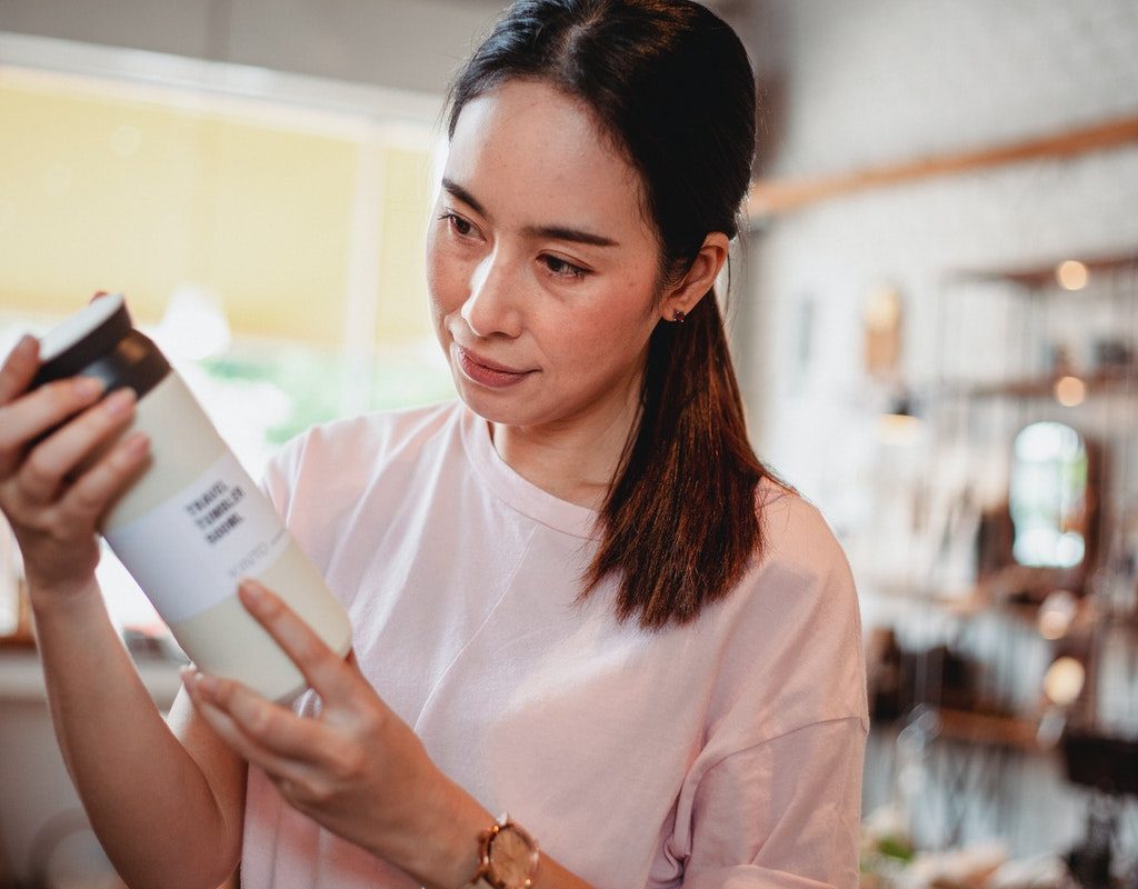 A woman looking at a beauty product, reading the label
