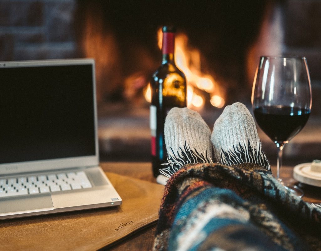 a single person with their laptop, wine, and blanket relaxing