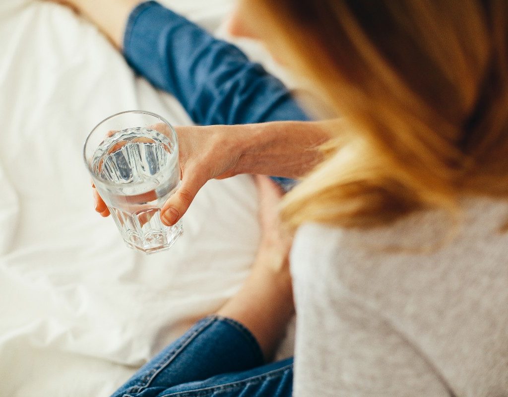 woman-drinking-water-on-white-blanket
