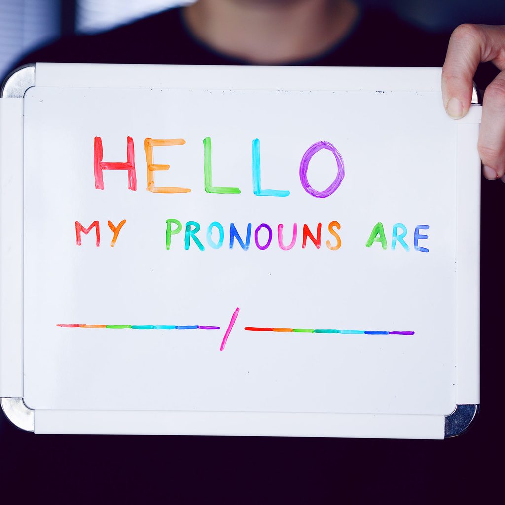 Person holding a sign declaring pronouns