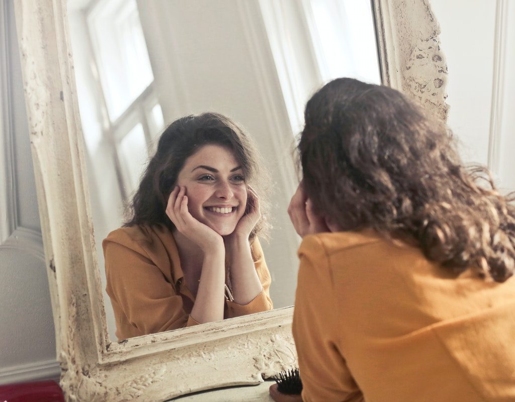A woman smiling at her reflection in a mirror.