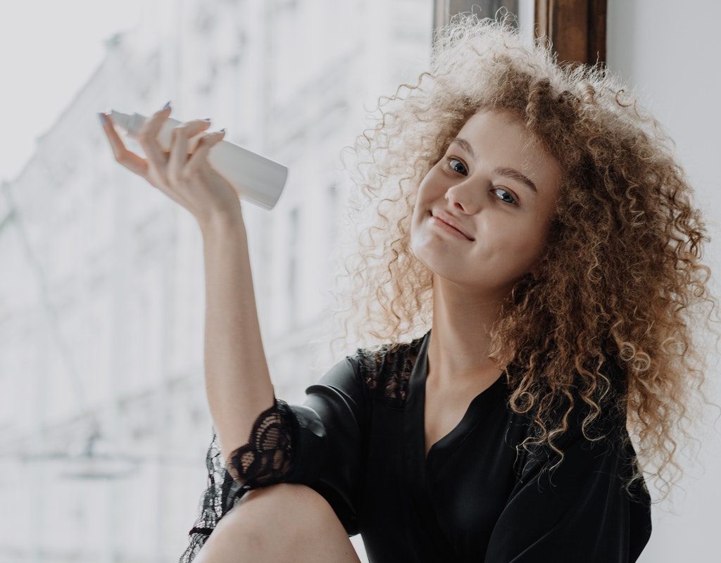 A female holding a hair spray in her hand.
