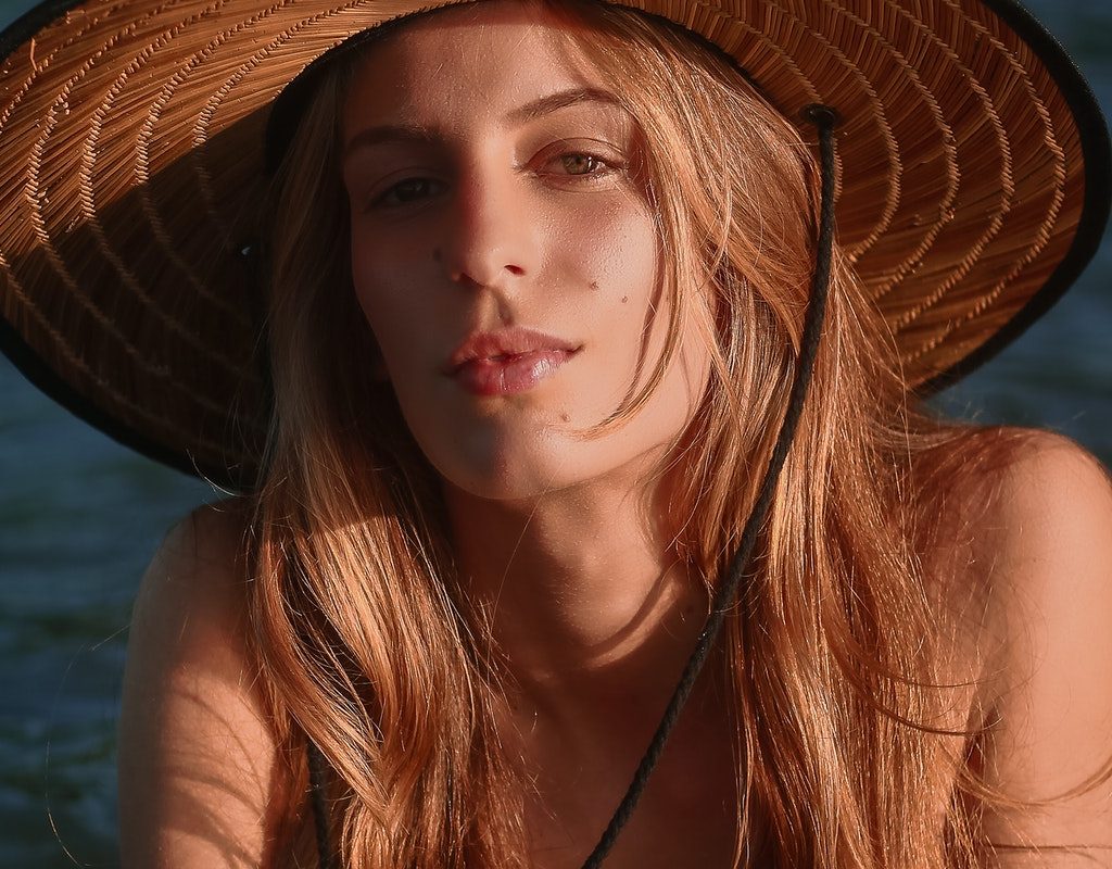 A woman wearing a straw sun hat with long, beachy, wavy hair.