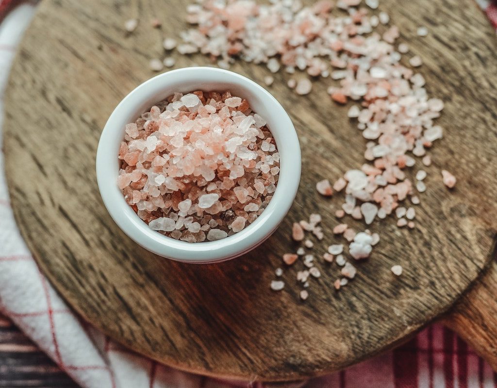 Pink salt in a bowl on wooden board on a table.