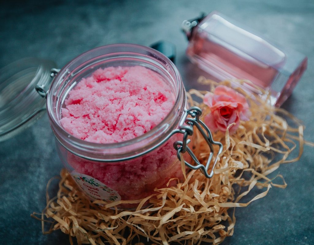 Pink body scrub in a clear jar on a table.