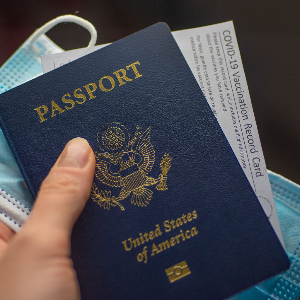 Person holding a passport, vaccination card, and mask