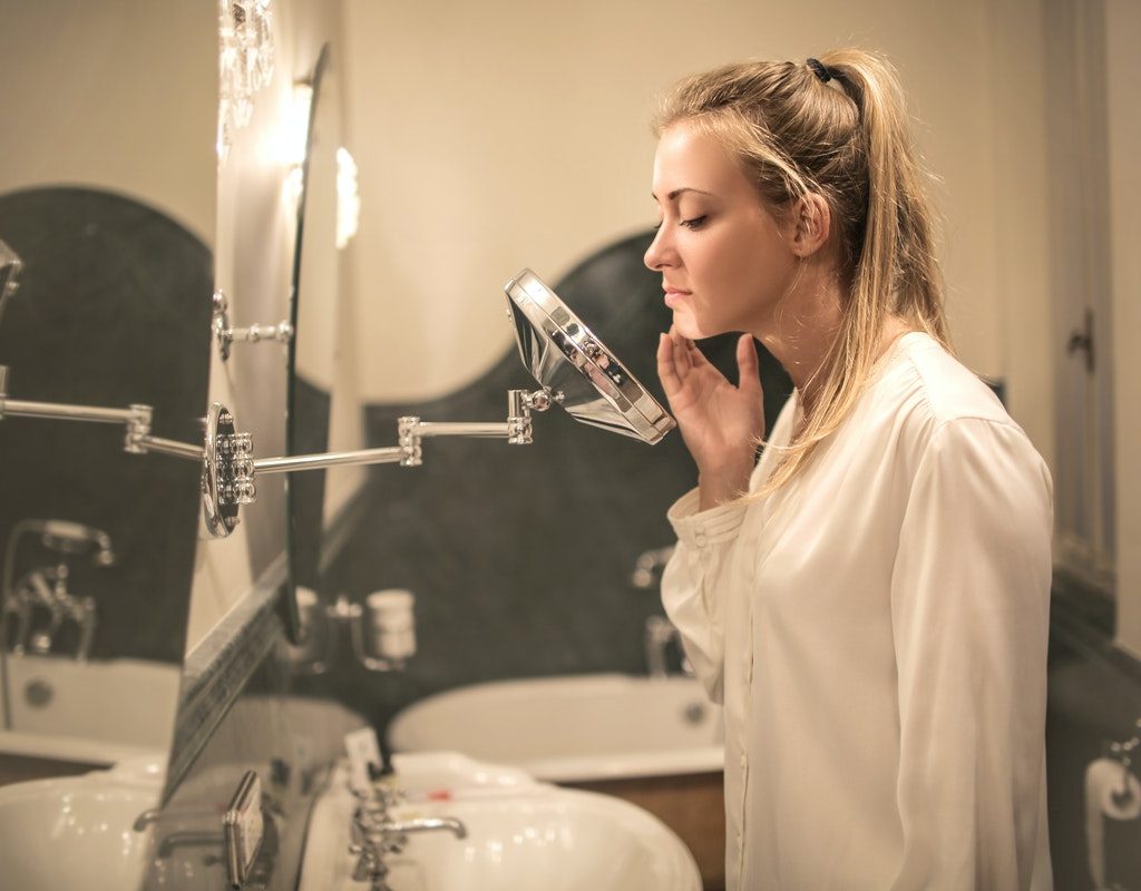 A female looking at her face in a mirror in her bathroom.