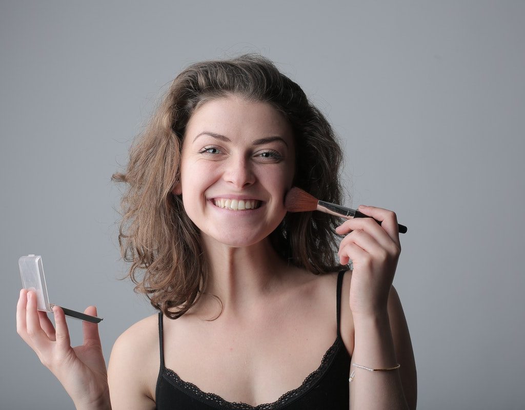 A woman smiling as she puts on her makeup.