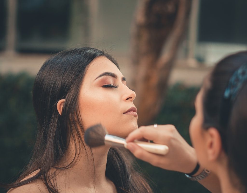 A woman is having her makeup applied by another woman using a makeup brush.