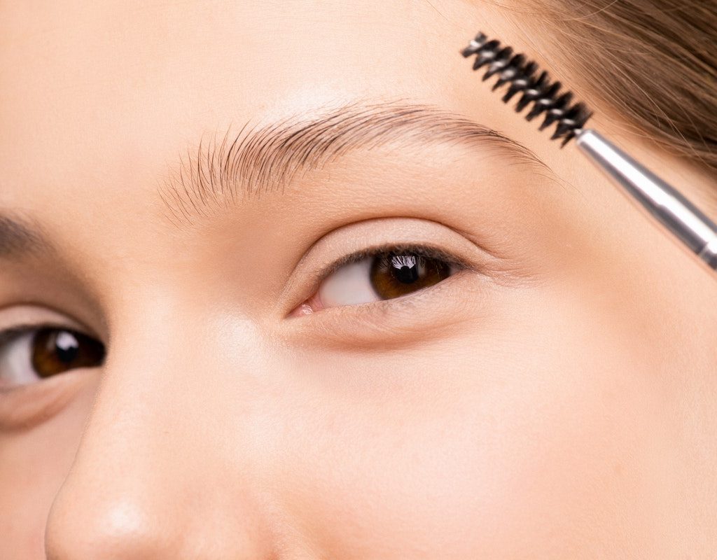 A woman holding a makeup wand up to her eye.