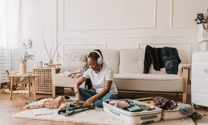 A woman is packing her suitcase while listening to music.
