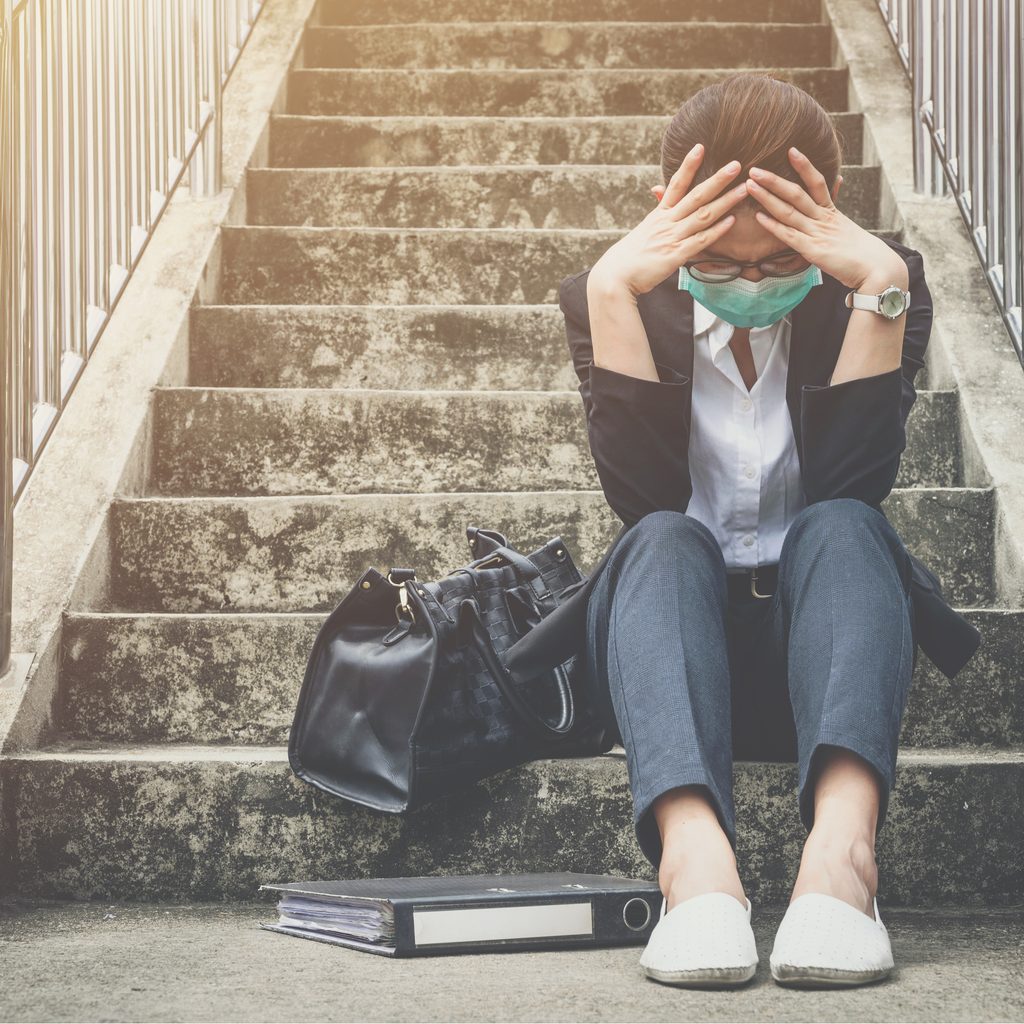 woman wearing mask sits on stairs with head in hands