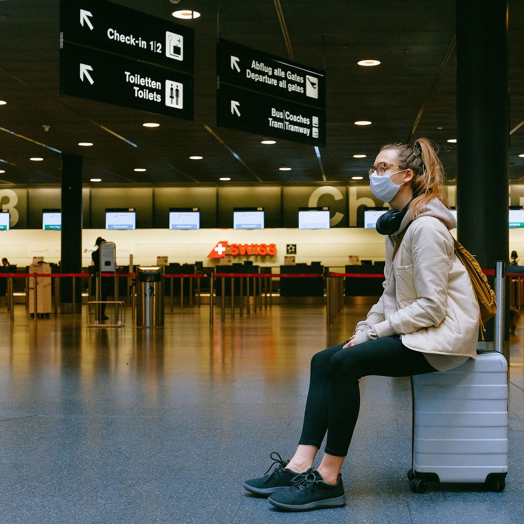 Woman wearing a mask sitting on suitcase in the airport