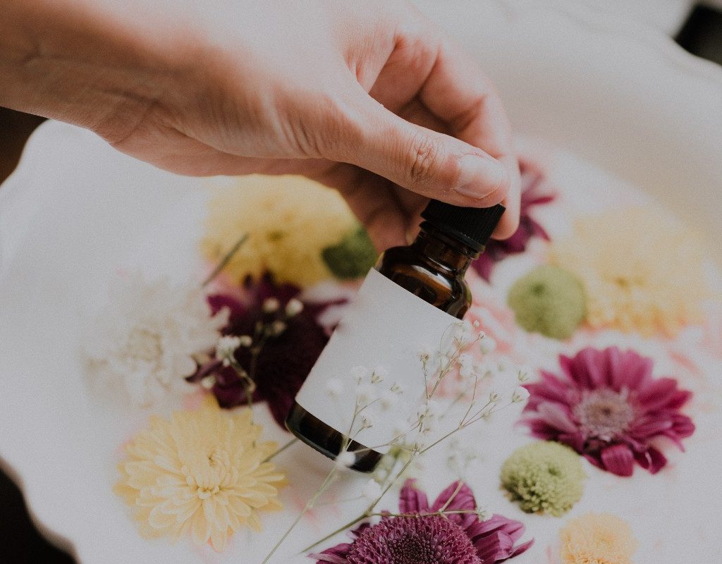 person holding a bottle of essential oil over a white basin with flowers