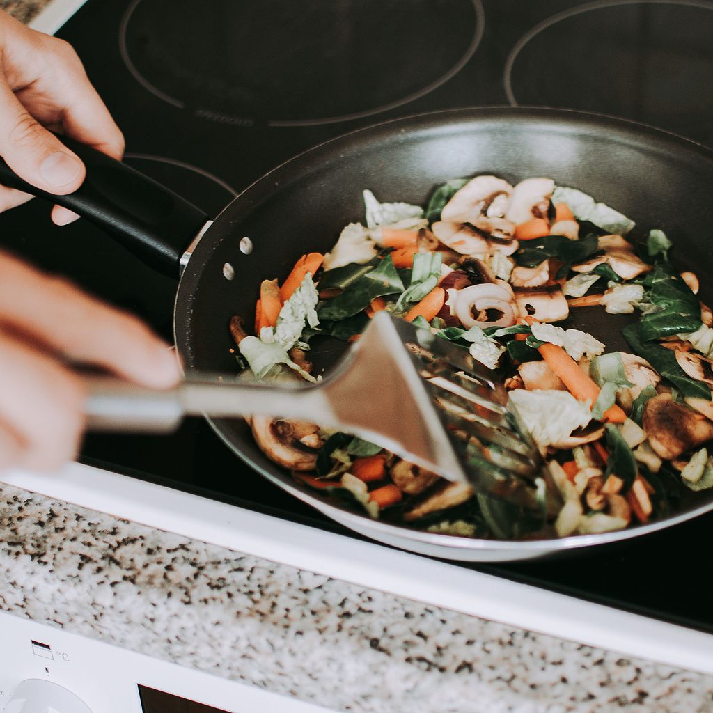 Person stir-frying vegetables on stove