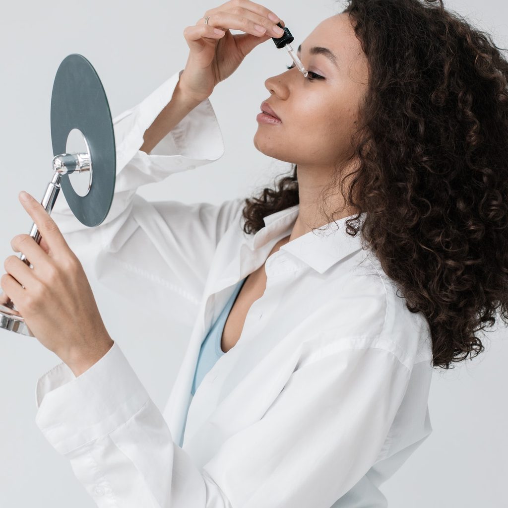 A woman putting face oil on while looking in a mirror.