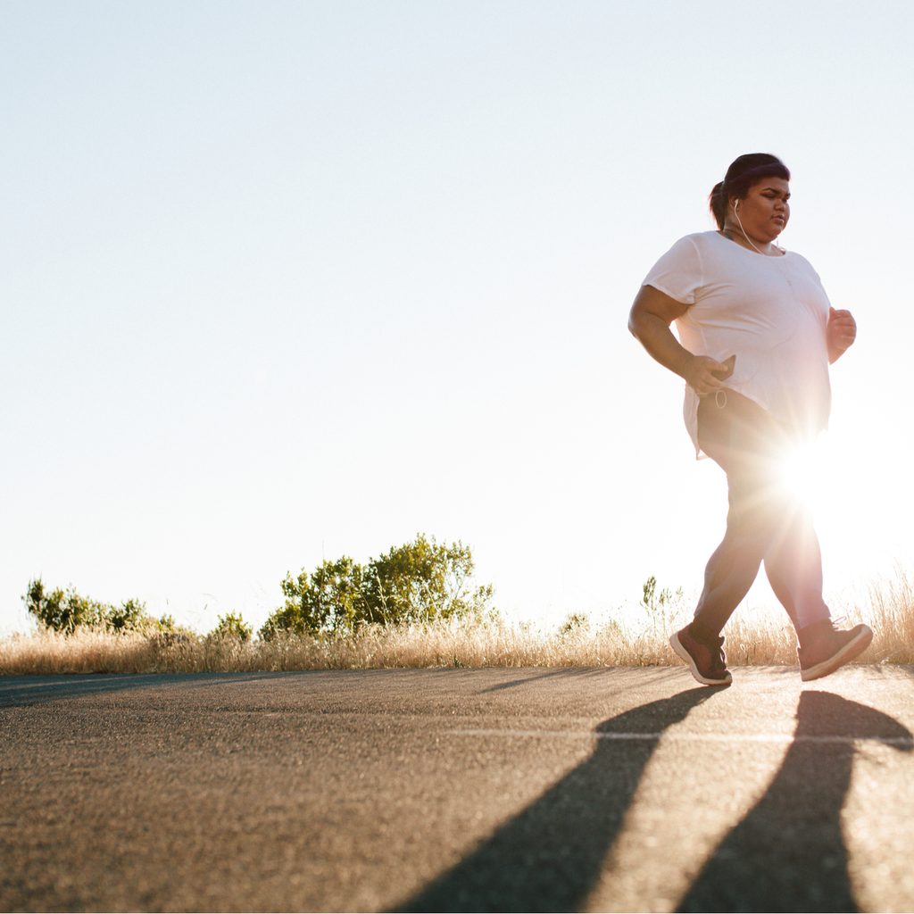 Woman listening to headphones walking at sunrise