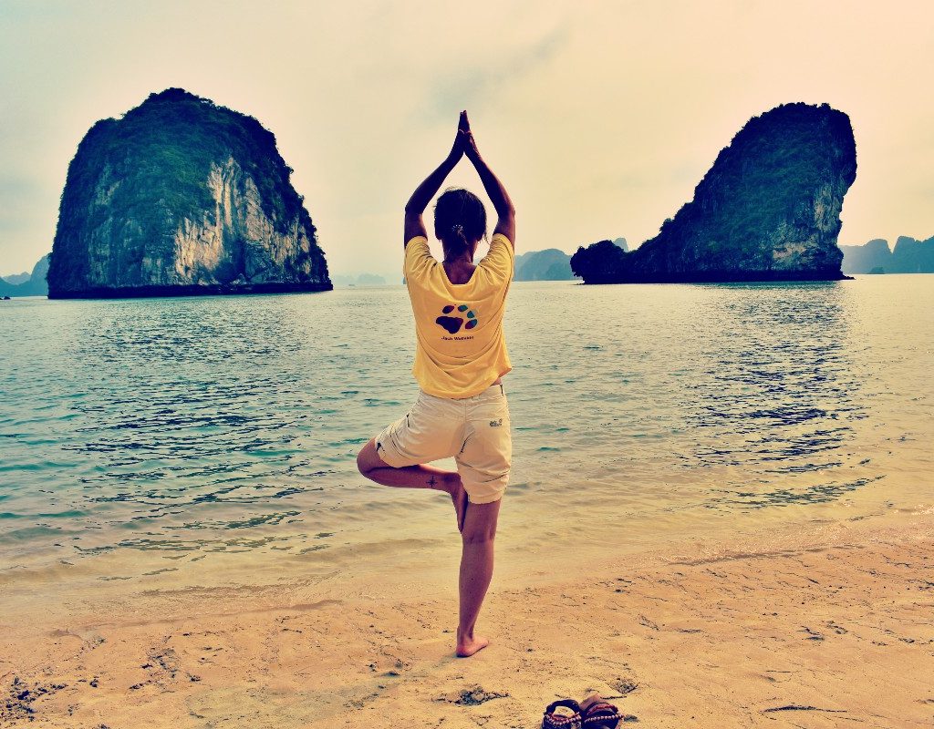 a woman doing tree pose on a beach