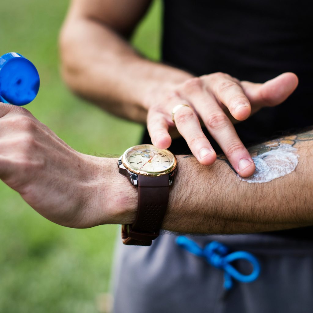 Closeup of man applying sunscreen to his arm outside in the grass