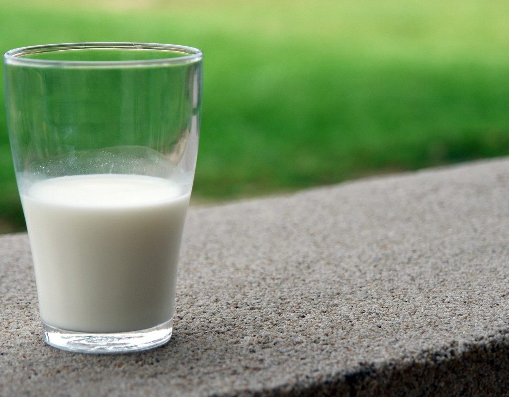 a glass half-full of milk on a concrete slab with grass in the background