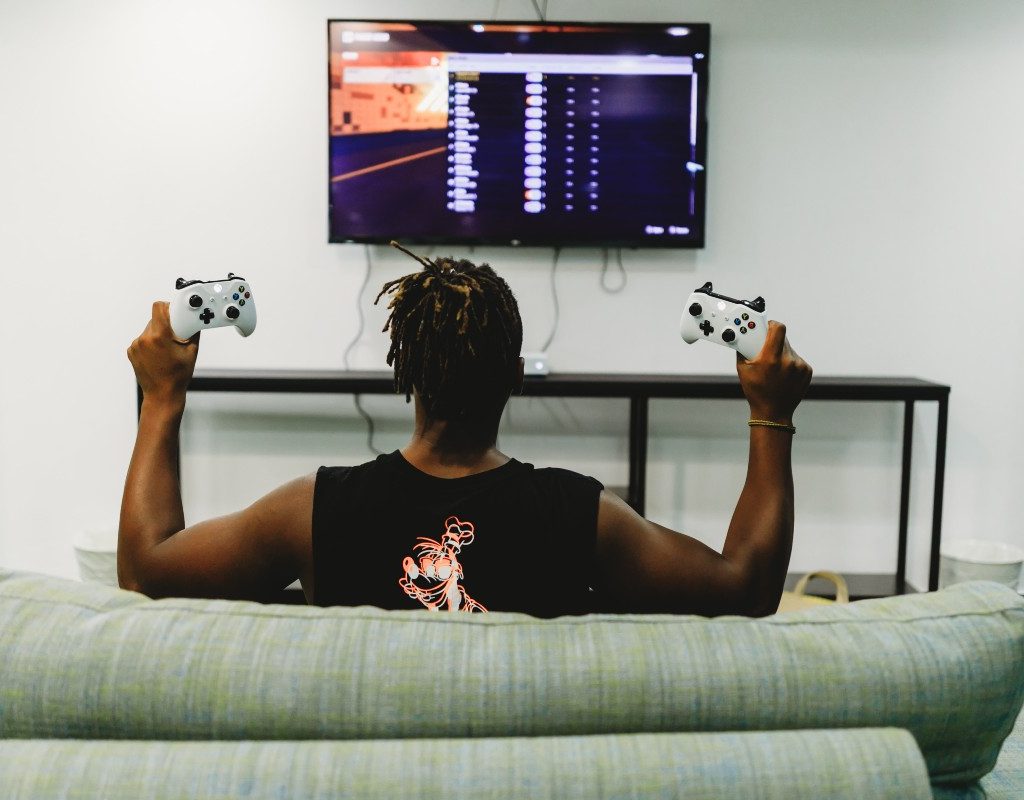 person with short hair sitting on green couch playing video games