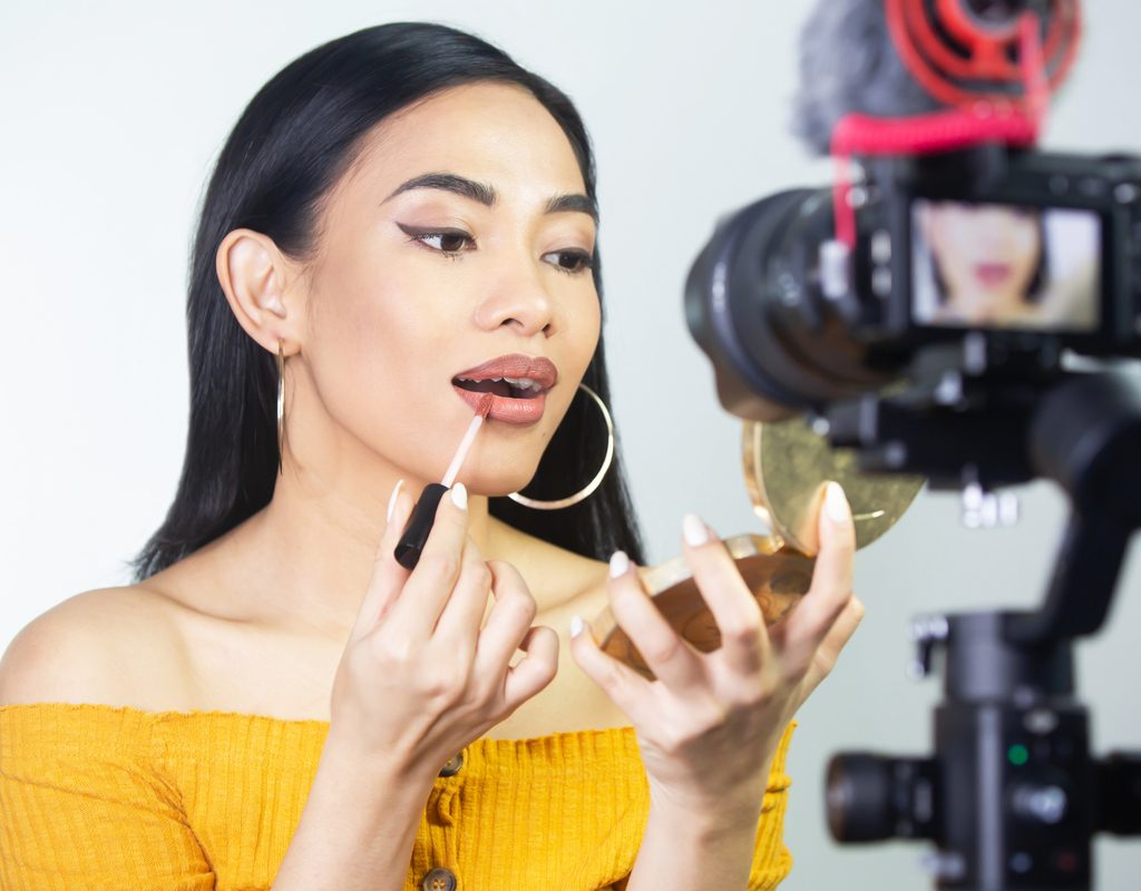 A woman putting on makeup in front of a camera.