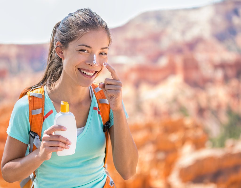 A woman putting sunscreen on her face while being out in the sun.