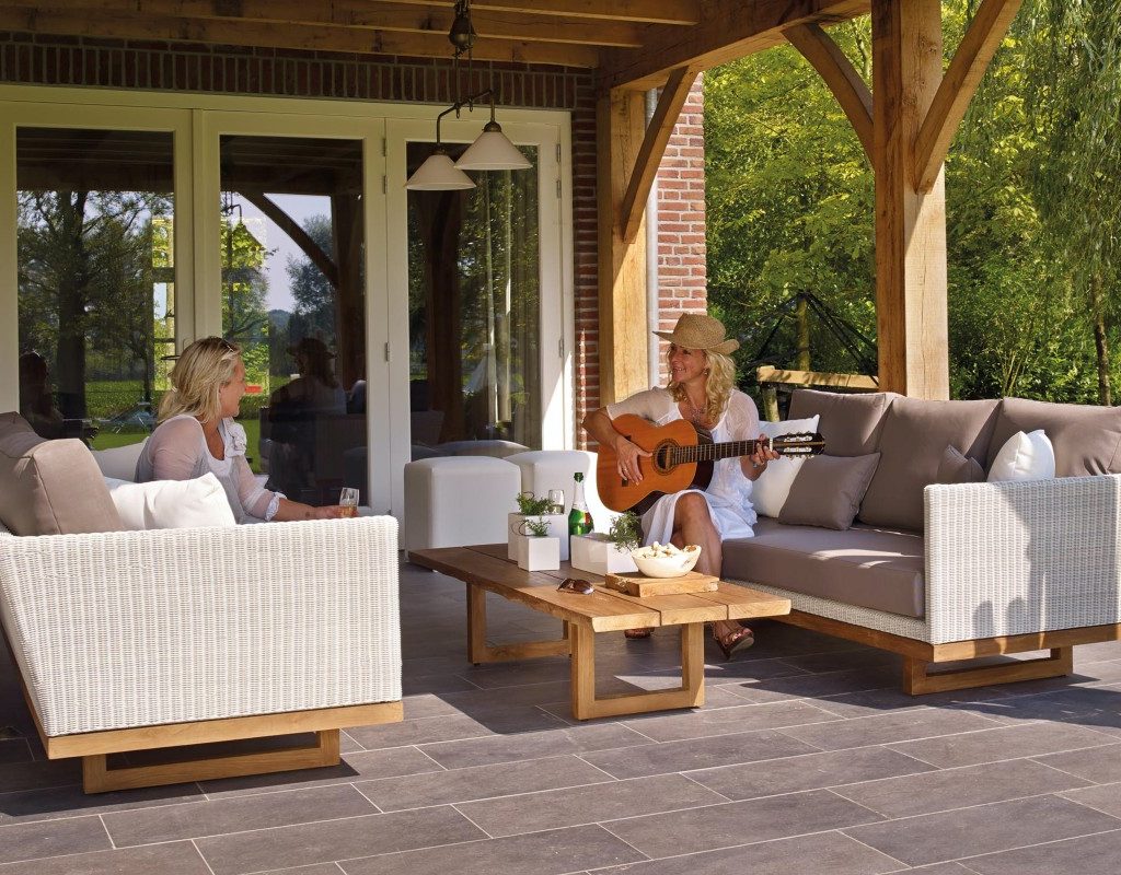 two women sitting outside on white furniture. one is playing the guitar