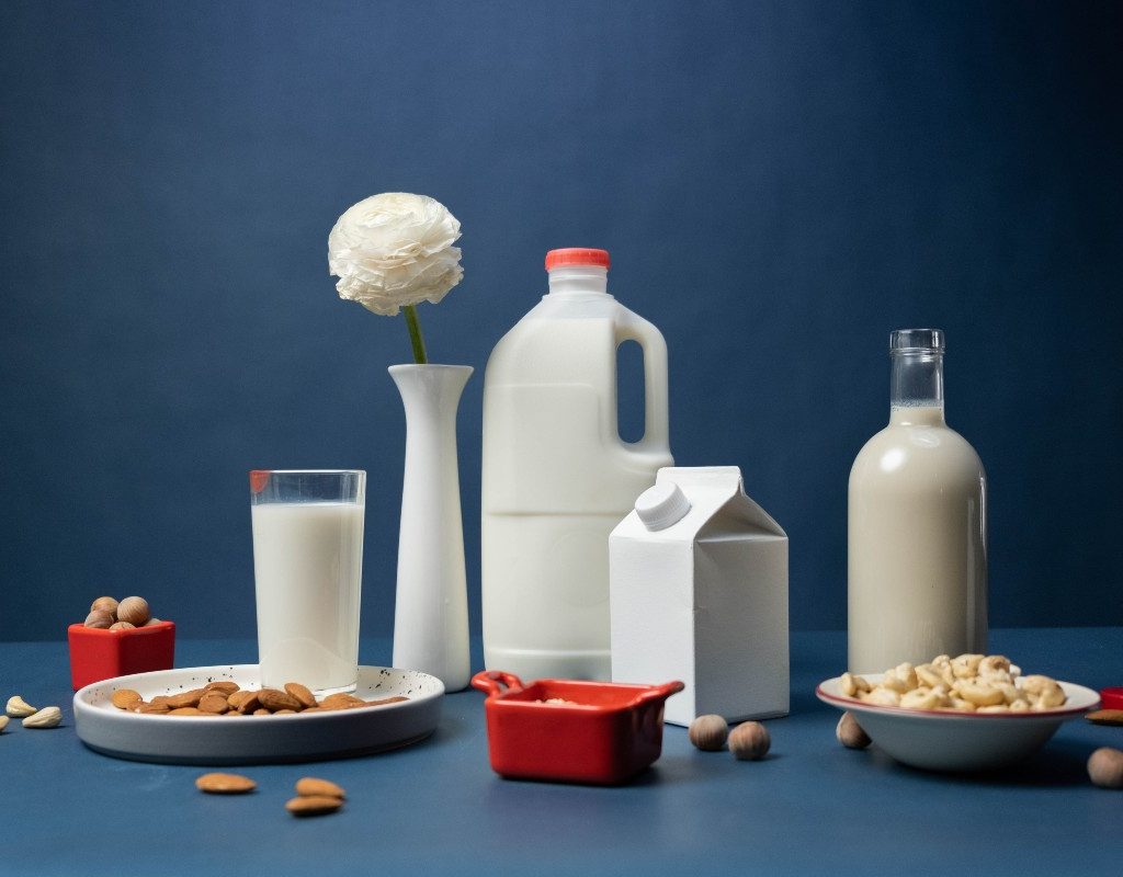 various sizes of milk containers and two bowls of nuts on a blue table with blue background