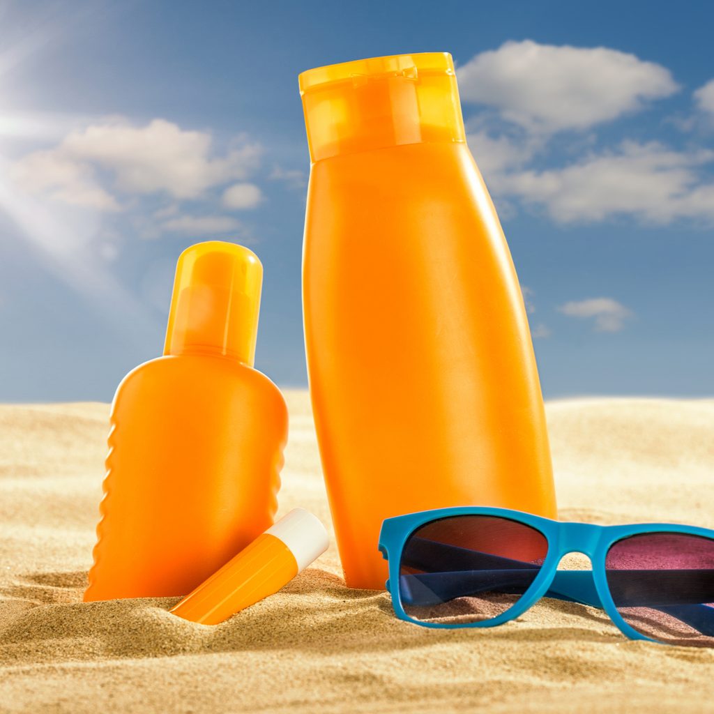 Various sunscreen products and sunglasses in the sand