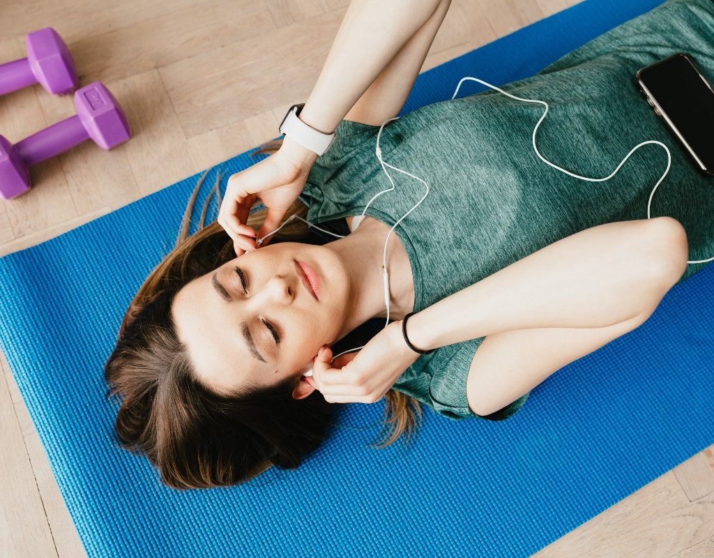 woman listening to music on blue yoga mat with purple hand weights nearby