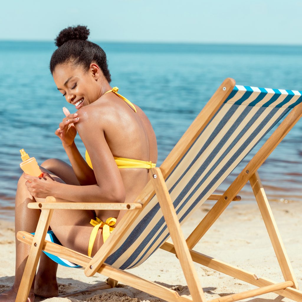Woman sitting in beach chair applying sunscreen