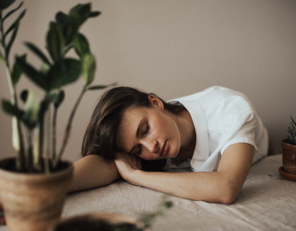 woman in a white top sleeping on a table surrounded by plants