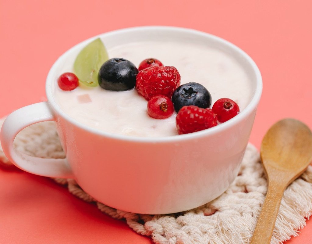yogurt and berres in a white mug on a pink-orange background