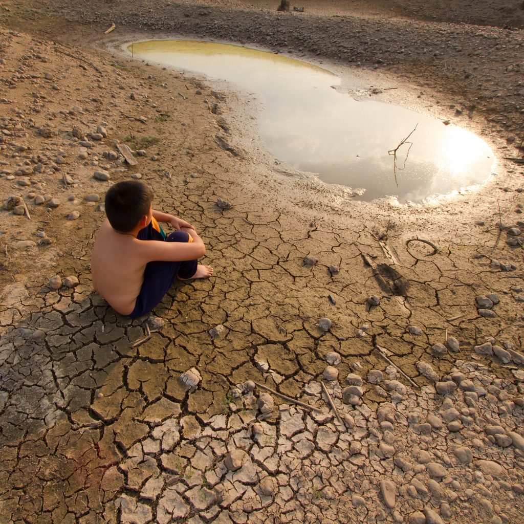 child sitting on dry, cracked ground looking at small pool of water