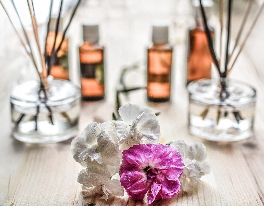 two essential oil reed diffusers on wooden table with a pink and white flower