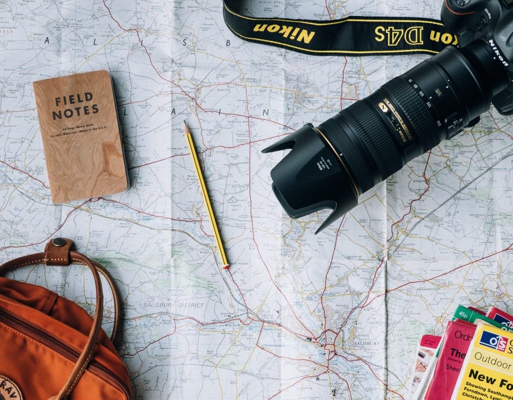 travel bag, books, camera, passport and writing instrument on top of a map
