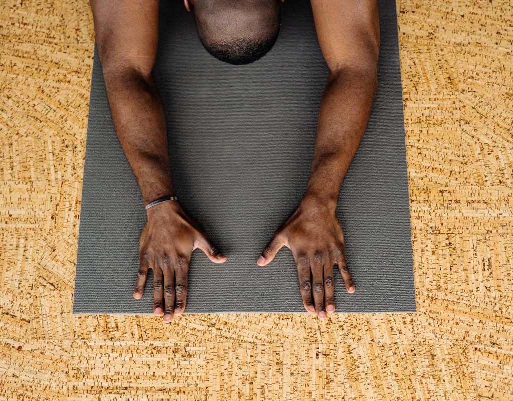 a man in child's pose on a black yoga mat