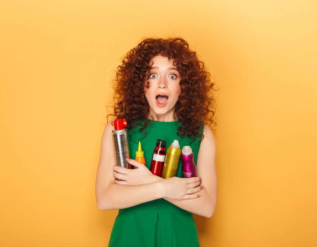 A curly haired woman holding a bunch of hair products.